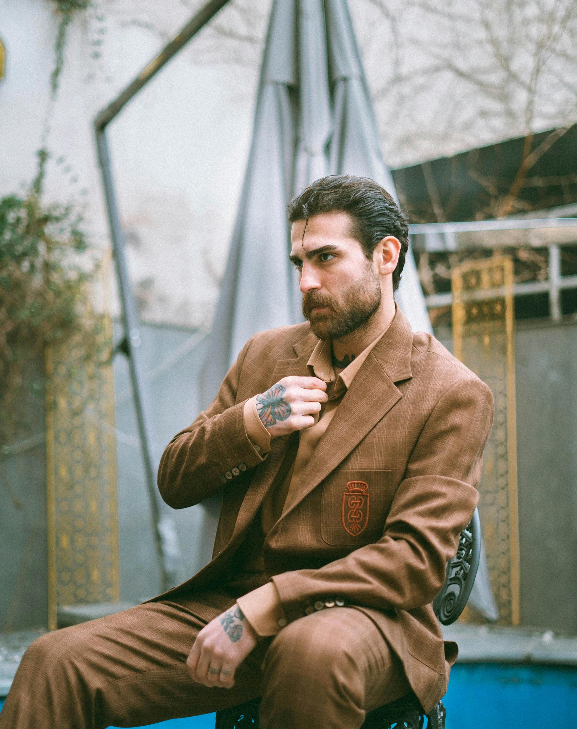 Man in a brown checkered suit seated outdoors